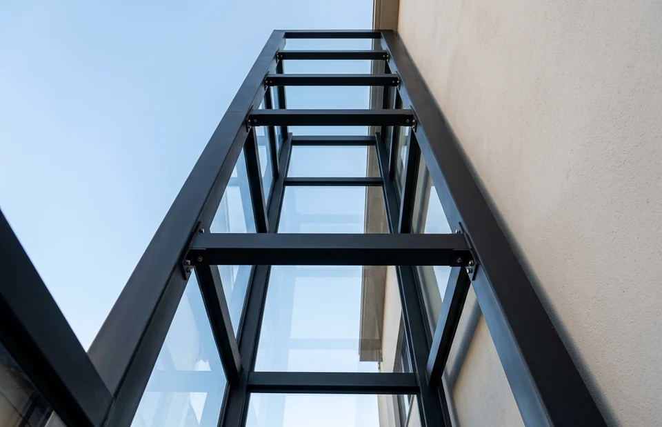 Detalhe de perfis metálicos e painéis de vidro de uma torre de elevador, visto de baixo